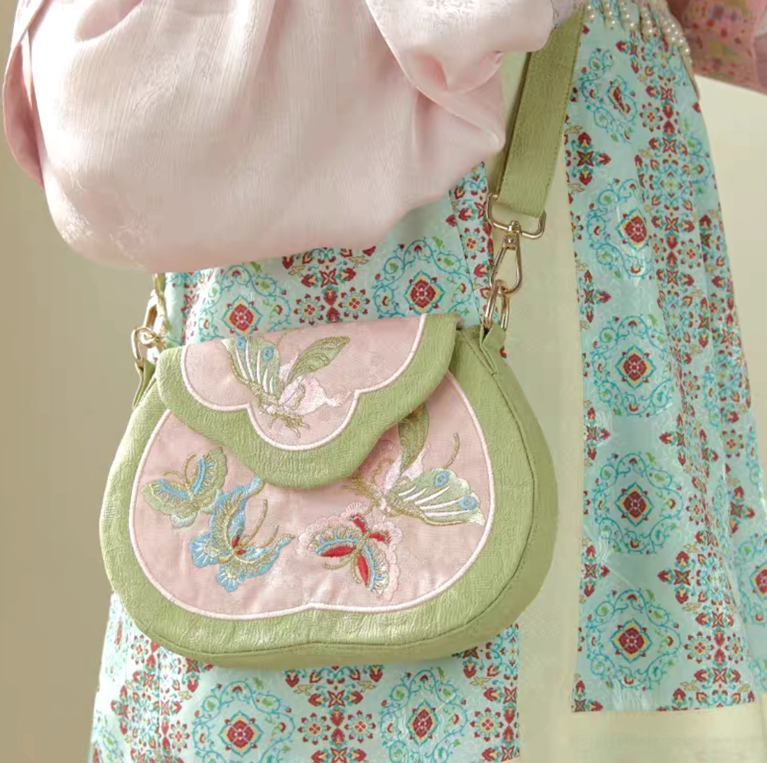 Tang-inspired butterfly embroidered Chinese crossbody bag worn with Hanfu traditional clothing, showing the blush pink saddle bag and sage green trim