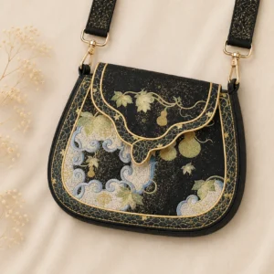 Tang-inspired black embroidered Chinese crossbody bag with gold gourd cloud motifs, gold piping, and glitter shoulder strap displayed on beige fabric