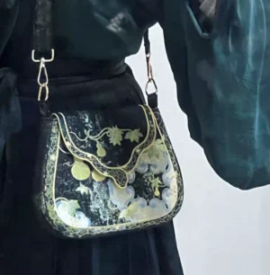 Traditional Chinese embroidered saddle crossbody bag worn with a dark green Hanfu skirt, showing gold gourd and cloud embroidery