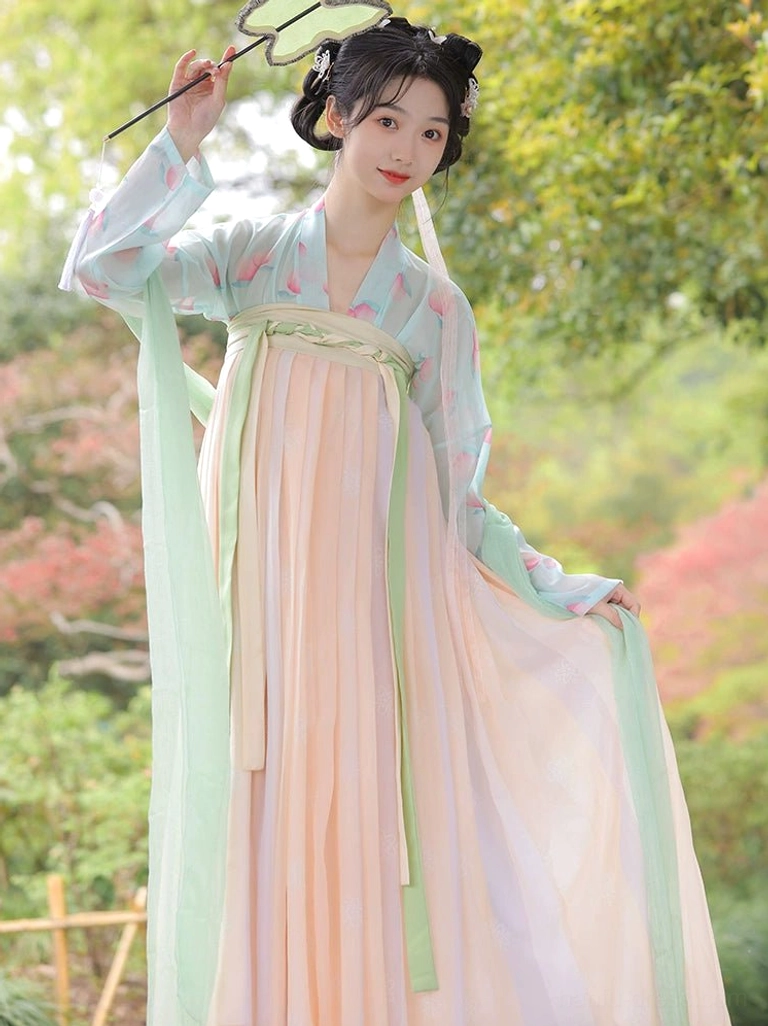 Front three-quarter view of a Tang-inspired Hanfu Qixiong Ruqun featuring an apricot pink gradient skirt, mint green printed blouse, and coordinated green ribbons
