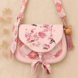 Front view of pink Tang-inspired Chinese crossbody bag with peach blossom and swallow embroidery, jacquard patchwork, bow strap, and gourd tassel