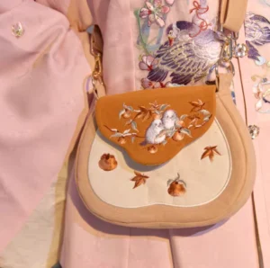 Tang-inspired sparrow and persimmon embroidered Chinese crossbody bag worn with pink floral Hanfu front close-up