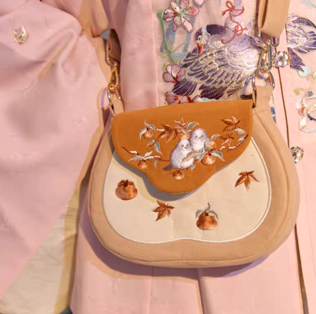 Tang-inspired sparrow and persimmon embroidered Chinese crossbody bag worn with pink floral Hanfu front close-up