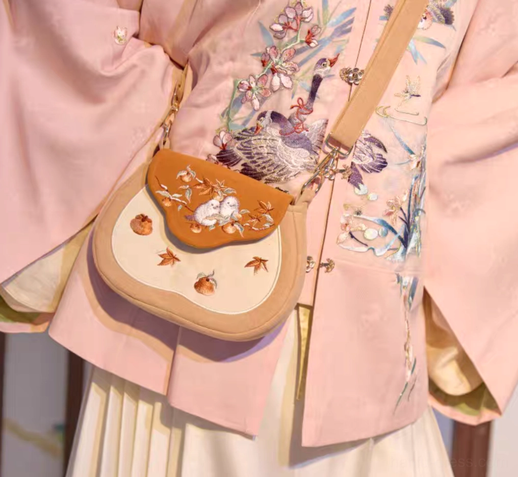Tang-inspired embroidered Chinese saddle crossbody bag with adjustable tan strap styled with pink Hanfu and pleated skirt