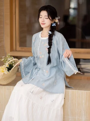 Seated side view of blue Tang style embroidered long sleeve top and white layered Hanfu midi skirt