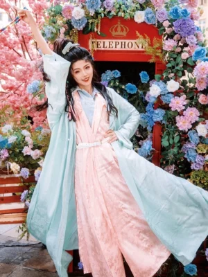 Mint green and peach pink Tang style Hanfu robe outfit photographed outdoors among flowers with flowing long sleeves and layered styling