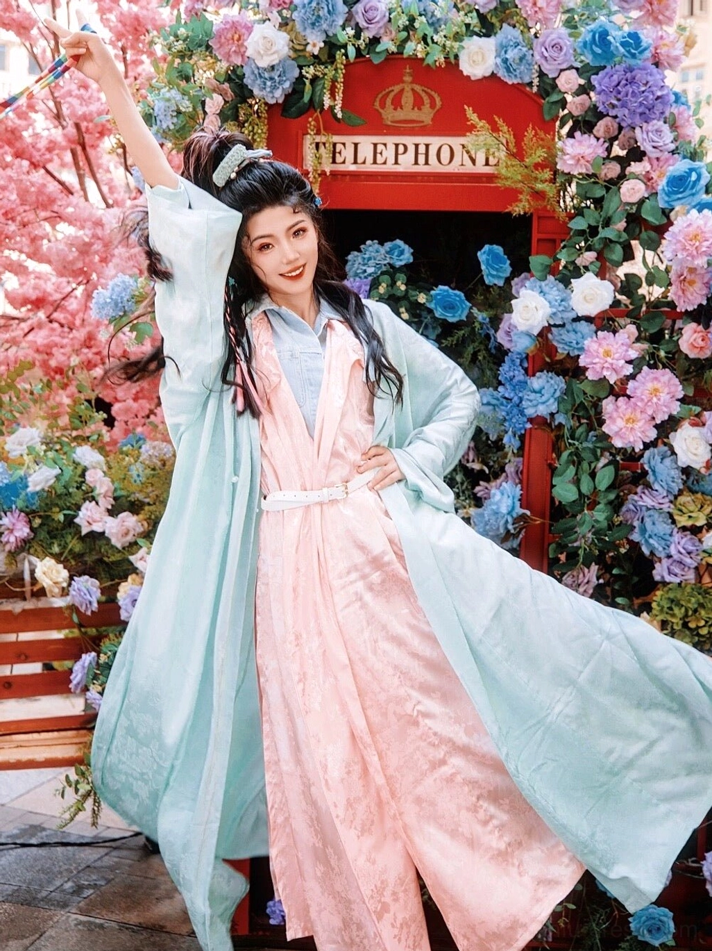 Mint green and peach pink Tang style Hanfu robe outfit photographed outdoors among flowers with flowing long sleeves and layered styling