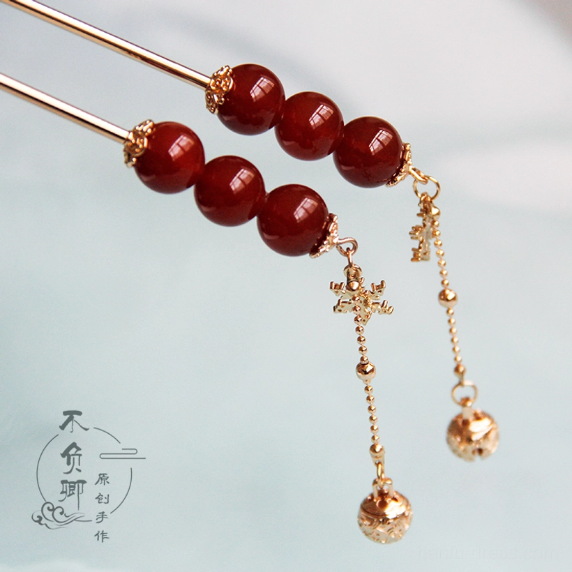 Tanghulu Chinese hair stick with deep red round beads gold-tone metal rod snowflake charm and dangling bell tassel on a light blue background