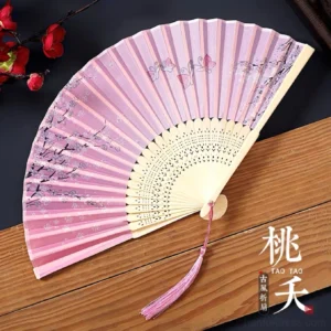Taoyao pink floral butterfly Chinese folding hand fan with hollow carved bamboo ribs and pink tassel displayed on dark wood