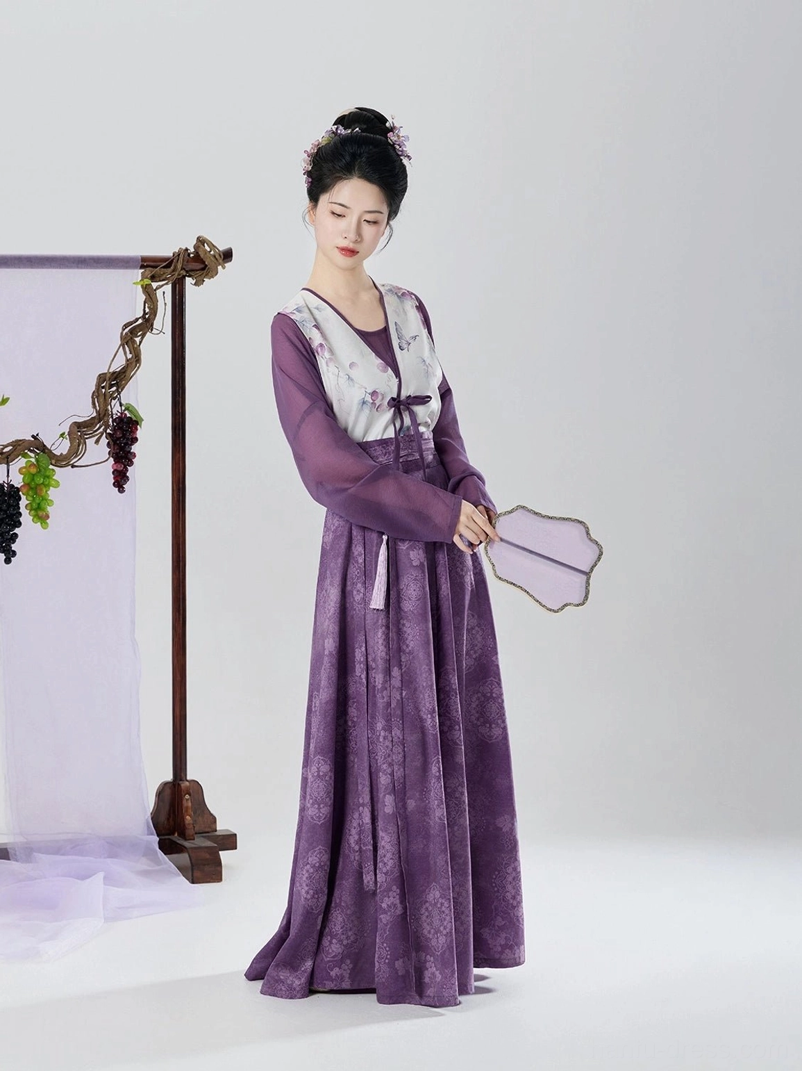 Back three-quarter view of Tang Dynasty inspired purple hanfu set with flowing pleated skirt and grape print beizi overlay