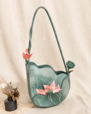 Teal lotus blossom Chinese shoulder bag with embroidered white lotus leaf veins, layered petal silhouette, three-dimensional pink lotus flower and matching shoulder strap on a linen background