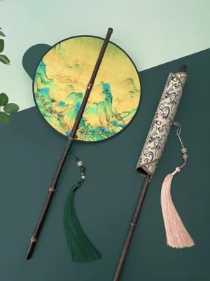 Traditional Chinese round hand fan with A Thousand Li of Rivers and Mountains landscape artwork, dark bamboo handle, green tassel, decorative bead pendant, and matching vintage scroll storage sleeve