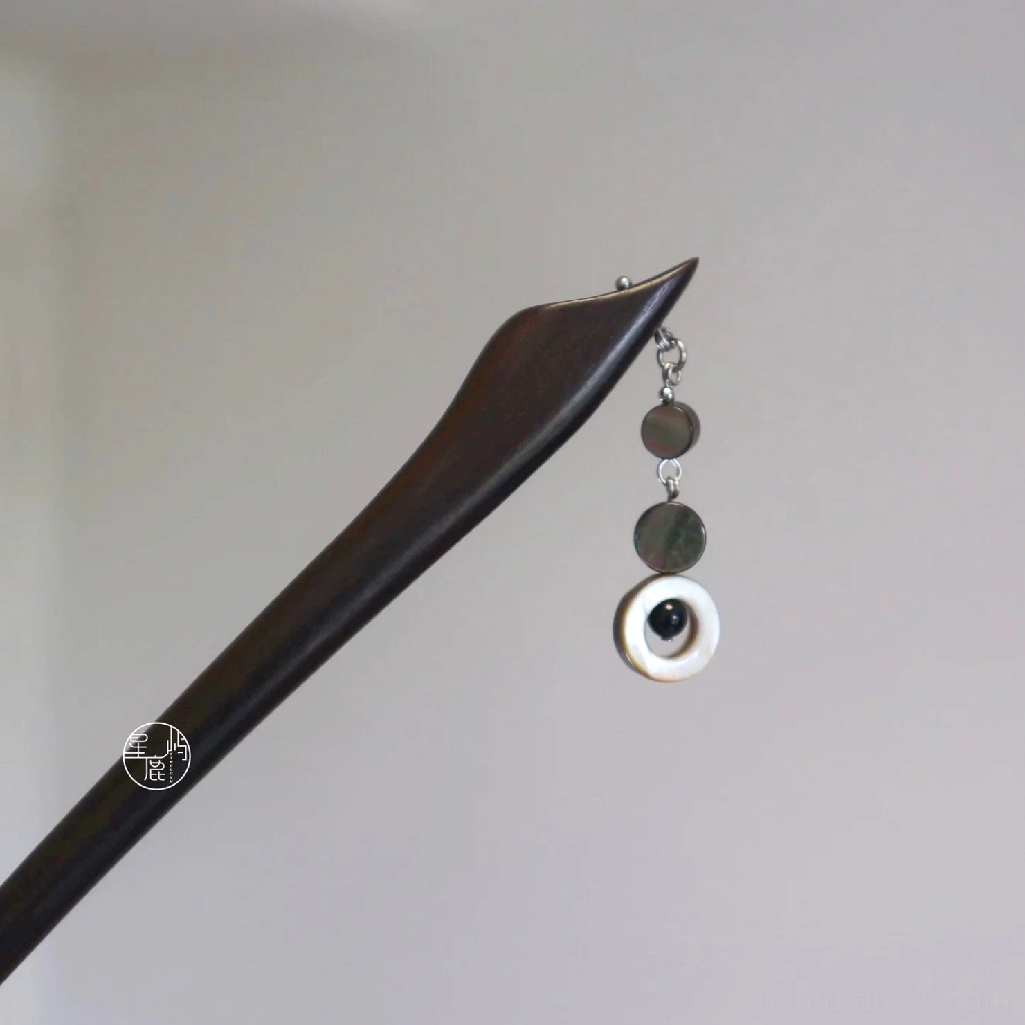 Dark wood Chinese hair stick with petal-shaped tip, shell drop, and traditional tassel ornament on a light gray background