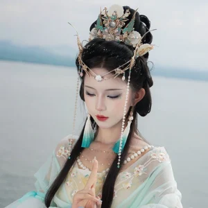 Tidal Sea Spirit Hanfu hair accessory complete set worn by model in light green embroidered Hanfu beside a lake, featuring gold crown, blue ornaments, pearl forehead chain and tassel details