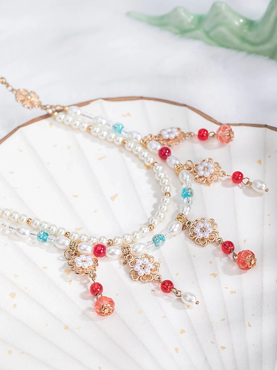 Traditional Chinese beaded Hanfu necklace displayed on a white gilt folding fan, with gold decorative hardware, white pearls, red and turquoise beads, flower pendants, and dangling bead drops