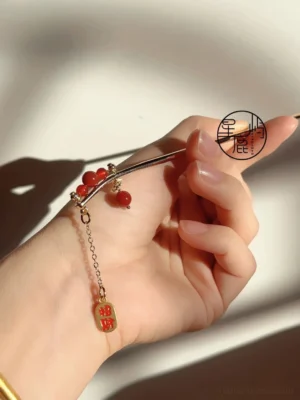 Hand held close up of traditional Chinese hair stick with red beads engraved blessing charm and delicate chain tassel