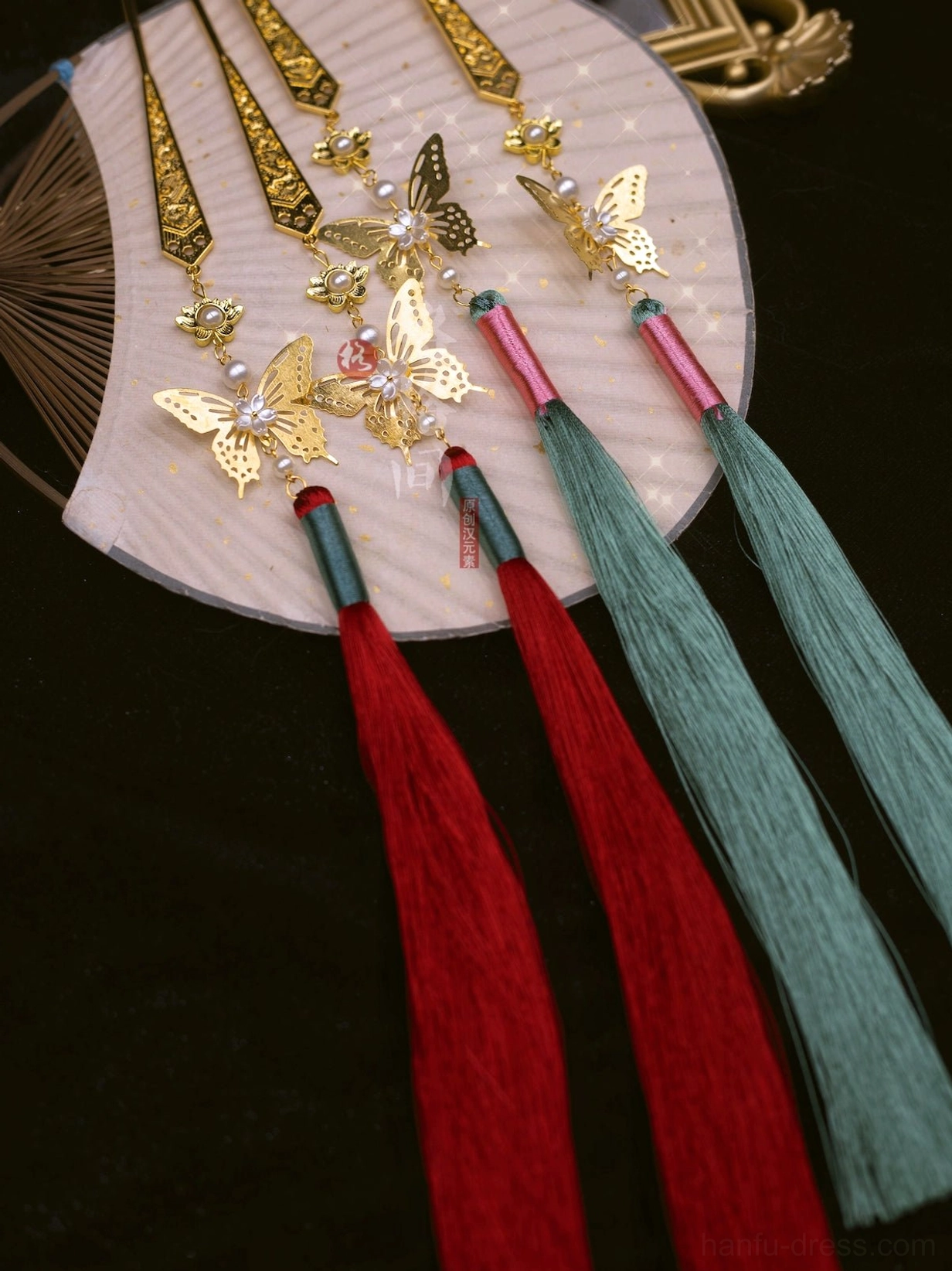 Traditional Chinese butterfly tassel hair pins in red and green displayed with a decorative Chinese folding fan