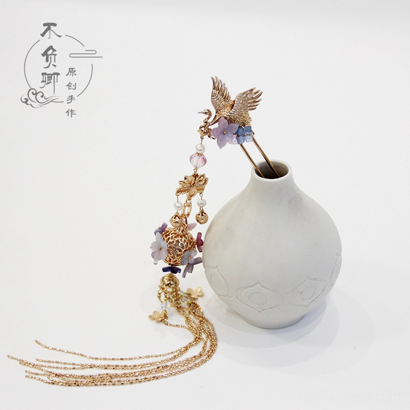 Traditional Chinese crane hair stick with glowing golden lantern pendant, purple flower accents, layered chains, and tassel displayed beside a ceramic vase