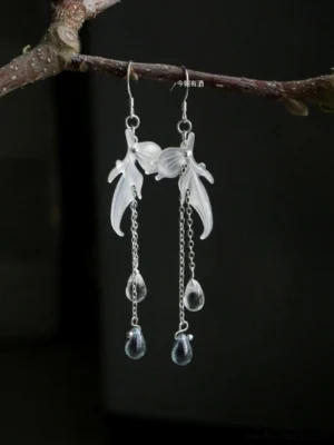 Close-up of traditional Chinese fairy style Hanfu earrings featuring pearly white goldfish pendants, silver chains, clear beads, and deep blue teardrop charms