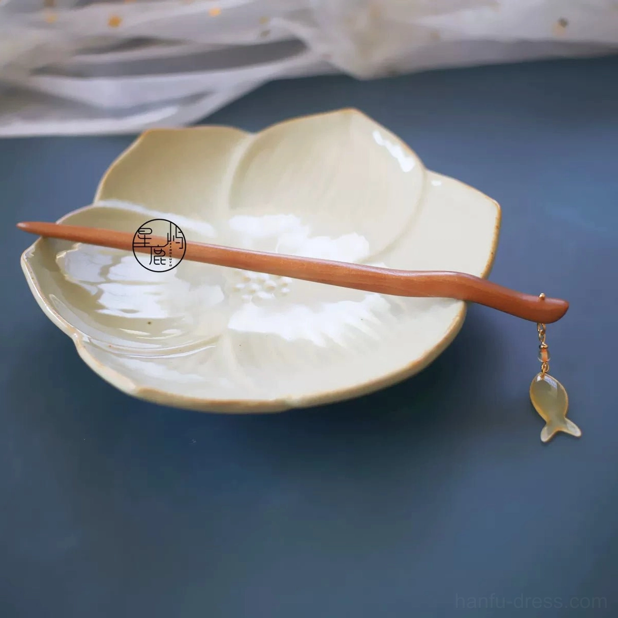 Traditional Chinese fish drop hair stick with sleek curved wooden body and compact translucent pendant on ceramic dish