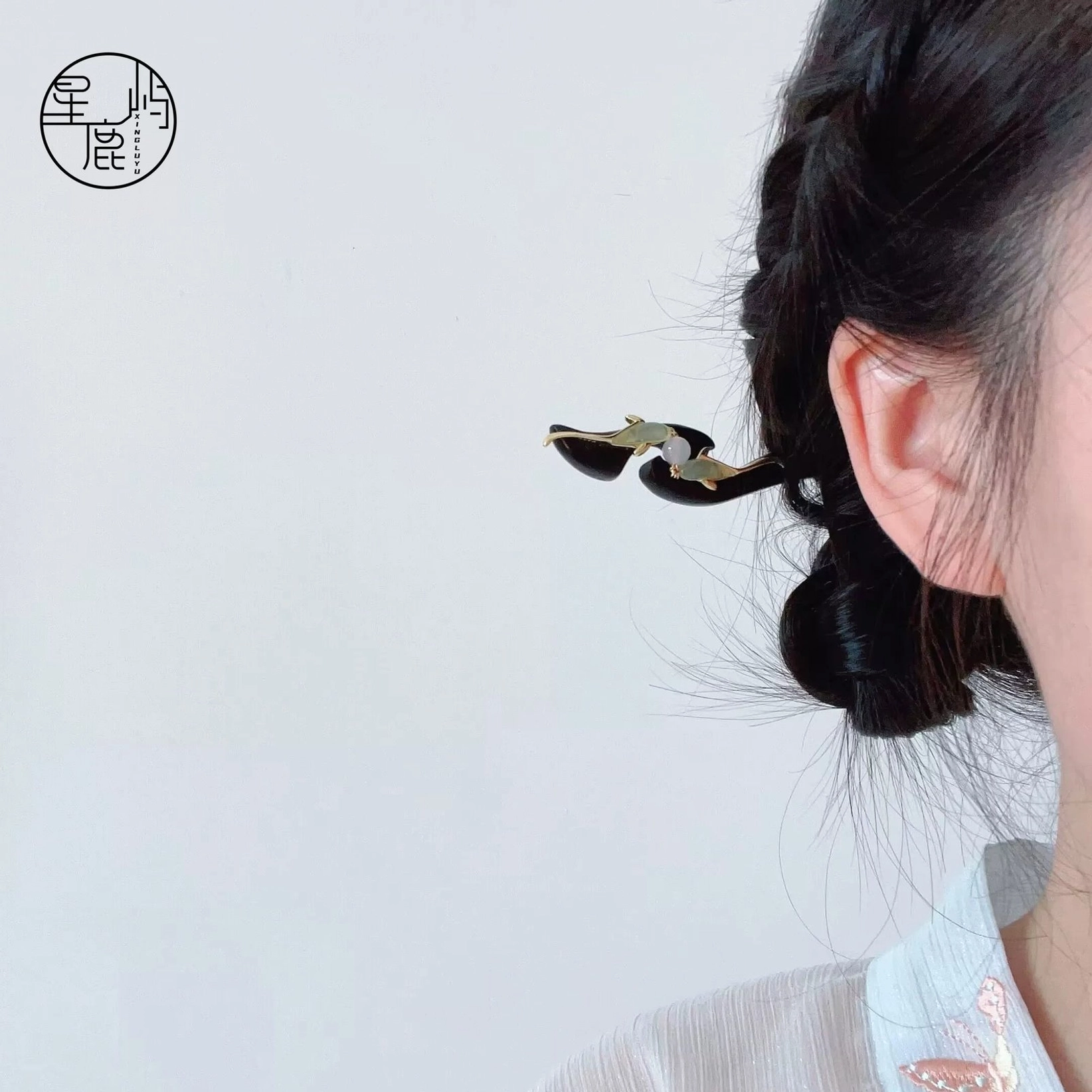Woman wearing a traditional Chinese fish hair stick in a coiled bun with a black wooden shaft, gold fish ornaments, green jade-style accents, and white bead