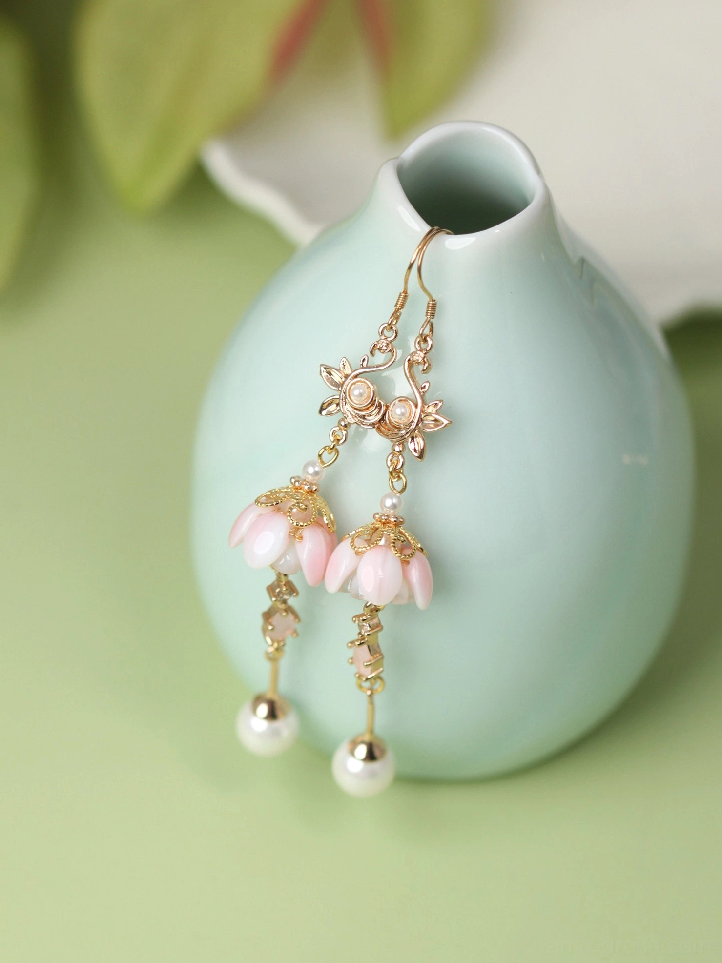 Traditional Chinese flower earrings hanging on a celadon vase with pink blossom pendants, gold chain links and pearl charms