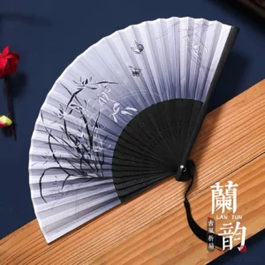 Traditional Chinese folding fan with grey orchid and butterfly ink painting, black carved bamboo ribs, and hanging tassel displayed on a Chinese style wooden surface
