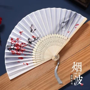Traditional Chinese folding hand fan with light gray fabric, red plum blossom and bird ink painting, carved beige bamboo ribs, and silver tassel displayed on a wooden strip against a dark blue background