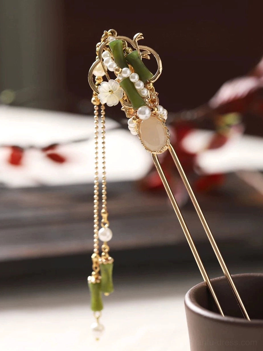 Front-left close-up of a traditional Chinese hair stick with green bamboo ornaments, white flower charms, faux pearl cluster, oval beige centerpiece, and coordinated hanging tassel