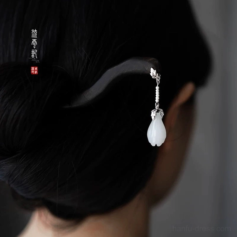 Woman wearing a traditional Chinese hair stick in an elegant low bun, featuring a dark wavy ebony shaft, silver floral detail, and white jade flower pendant