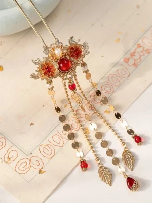 Traditional Chinese hair stick with layered tassels, gold floral ornament, red centerpiece, faux pearls, and leaf pendants photographed on vintage Chinese patterned paper