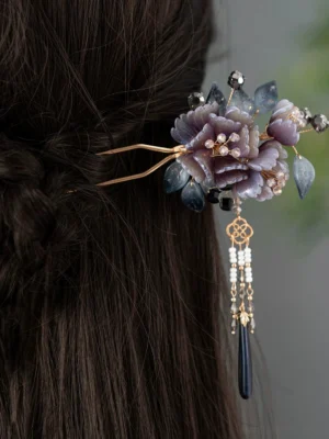 Traditional Chinese hair stick secured in a dark braided updo, showing the mauve peony flower, blue leaves, gold details, and hanging tassel