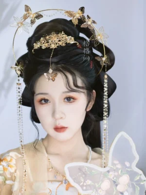 Front close-up of traditional Chinese Hanfu hair accessories with ornate gold butterfly crown, beaded side tassels, forehead charm, and Chinese hand fan