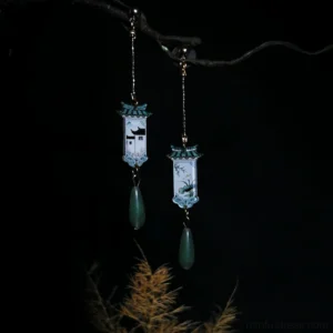 Traditional Chinese style Hanfu earrings with mismatched pendant designs, green roof-inspired accents, dangling teardrop charms, and delicate gold-toned chains on a rustic branch