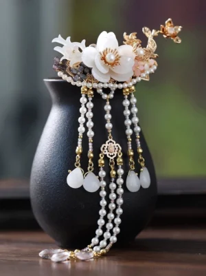 Traditional Chinese Hanfu floral hairpin with white flowers gold-tone ornaments pearl tassels and jade-tone pendant displayed on a black ceramic vase