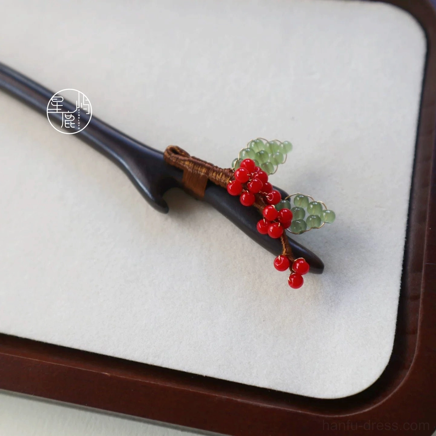 Traditional Chinese Hanfu hair stick displayed on a beige velvet cushion, featuring a smooth dark wood body, red and green bead ornaments, and wrapped brown twine