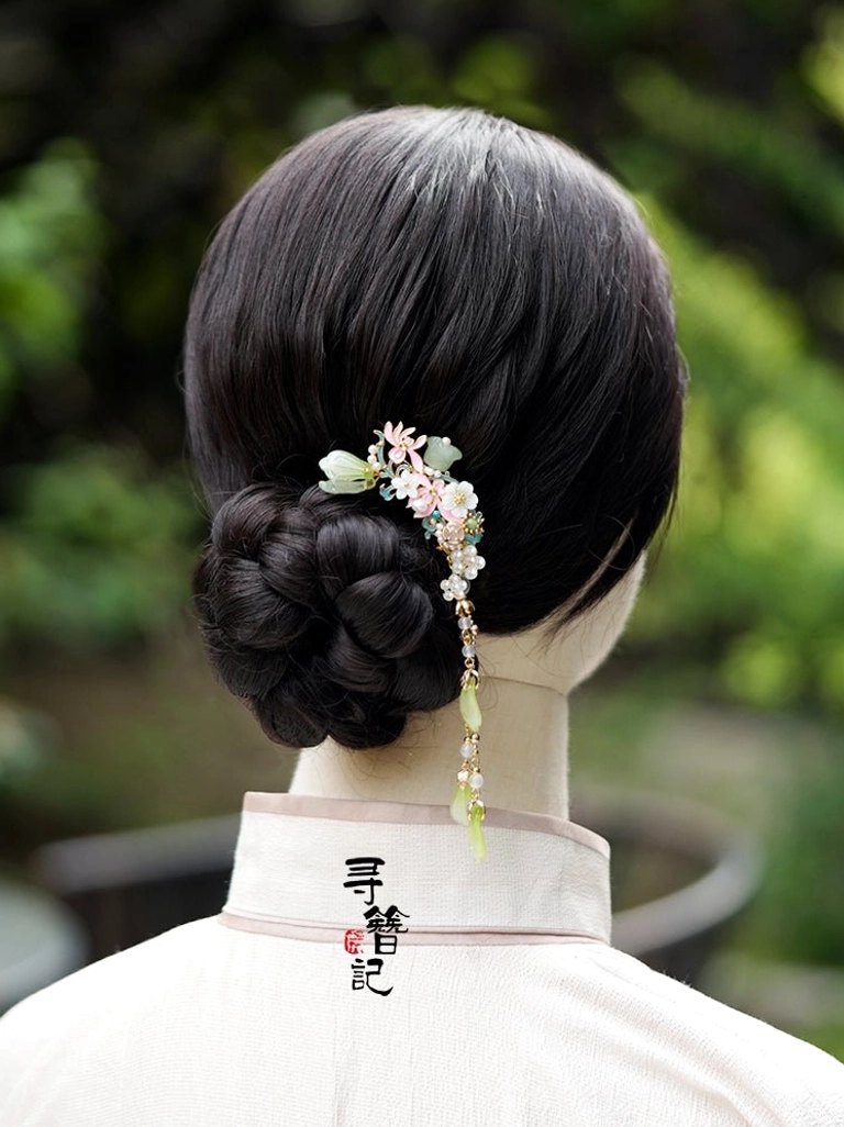 Model wearing a traditional Chinese floral Hanfu hairpin in a neat low bun, with a delicate green tassel hanging down the back of the neck in an outdoor garden setting