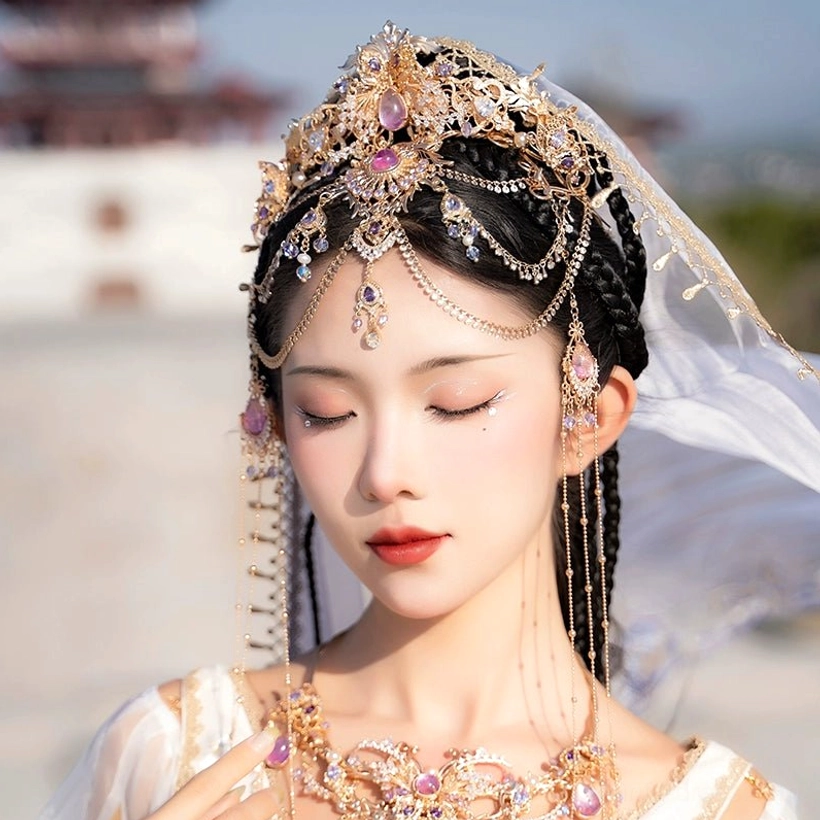 Traditional Chinese Hanfu head accessory crown with gold-tone floral details, pink-purple gemstones, and layered forehead and ear tassels worn with a white veil