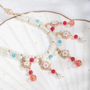 Traditional Chinese Hanfu layered beaded necklace displayed on a gilt white folding fan, featuring freshwater pearls, red and turquoise beads, gold filigree flower charms, and dangling pendant details