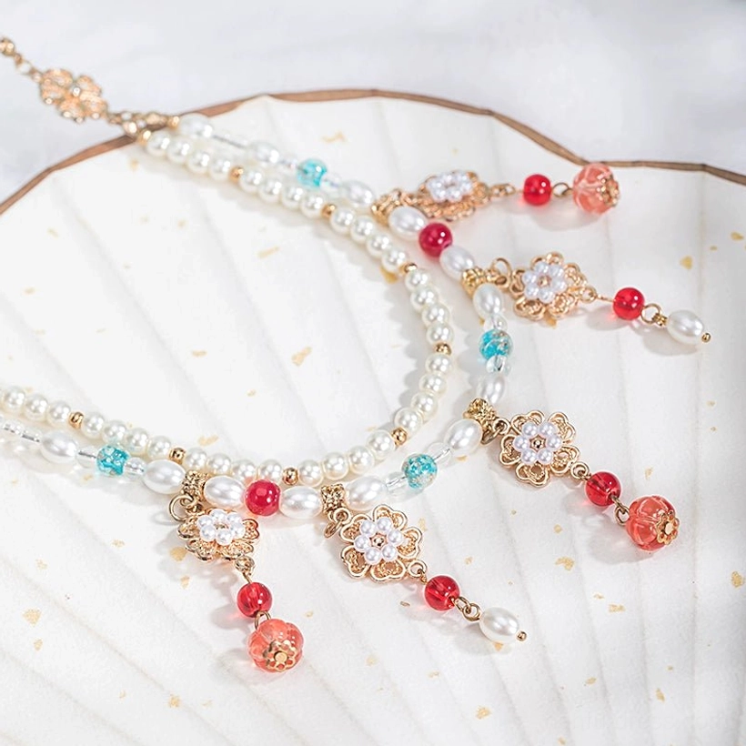 Traditional Chinese Hanfu layered beaded necklace displayed on a gilt white folding fan, featuring freshwater pearls, red and turquoise beads, gold filigree flower charms, and dangling pendant details