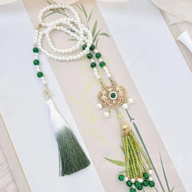Traditional Chinese Hanfu tassel pendant accessory with white pearl chains green jade-style beads ornate clasps and bamboo embroidery background