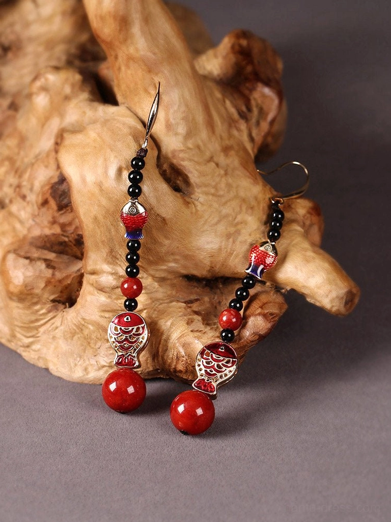Traditional Chinese koi fish earrings arranged on natural wood showing enamel fish ornaments layered bead chains and red pendant beads