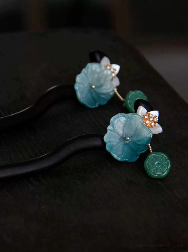 Pair of traditional Chinese lotus hair sticks displayed on dark wood with blue lotus flowers, white blossoms, gold accents, and green decorative pendants