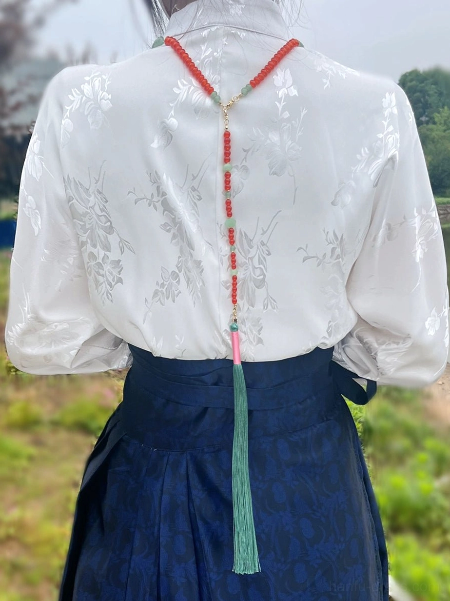 Back view of a woman wearing a traditional Chinese necklace with a long tassel hanging down the back over a coordinated Hanfu outfit