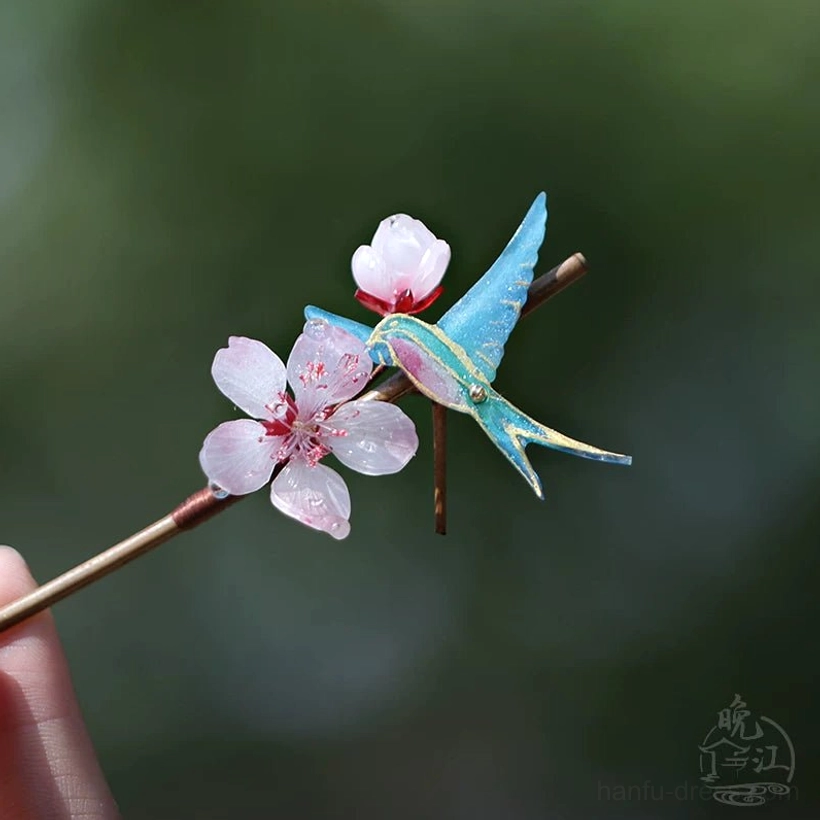 Low-angle detail of a traditional Chinese hair pin with swallow and peach blossom decorations on a slender brown hair stick