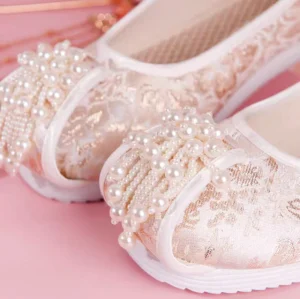 Close-up of traditional Chinese pearl Hanfu shoes showing delicate pearl tassel toe embellishments, floral jacquard texture, breathable fabric lining, and smooth white rubber outsole