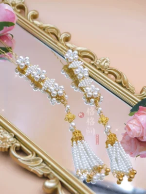 Top-down view of Chinese-inspired pearl tassel hair pins displayed on a vintage gold-framed mirror, showing clustered pearls, gold-tone details, and layered tassel pendants