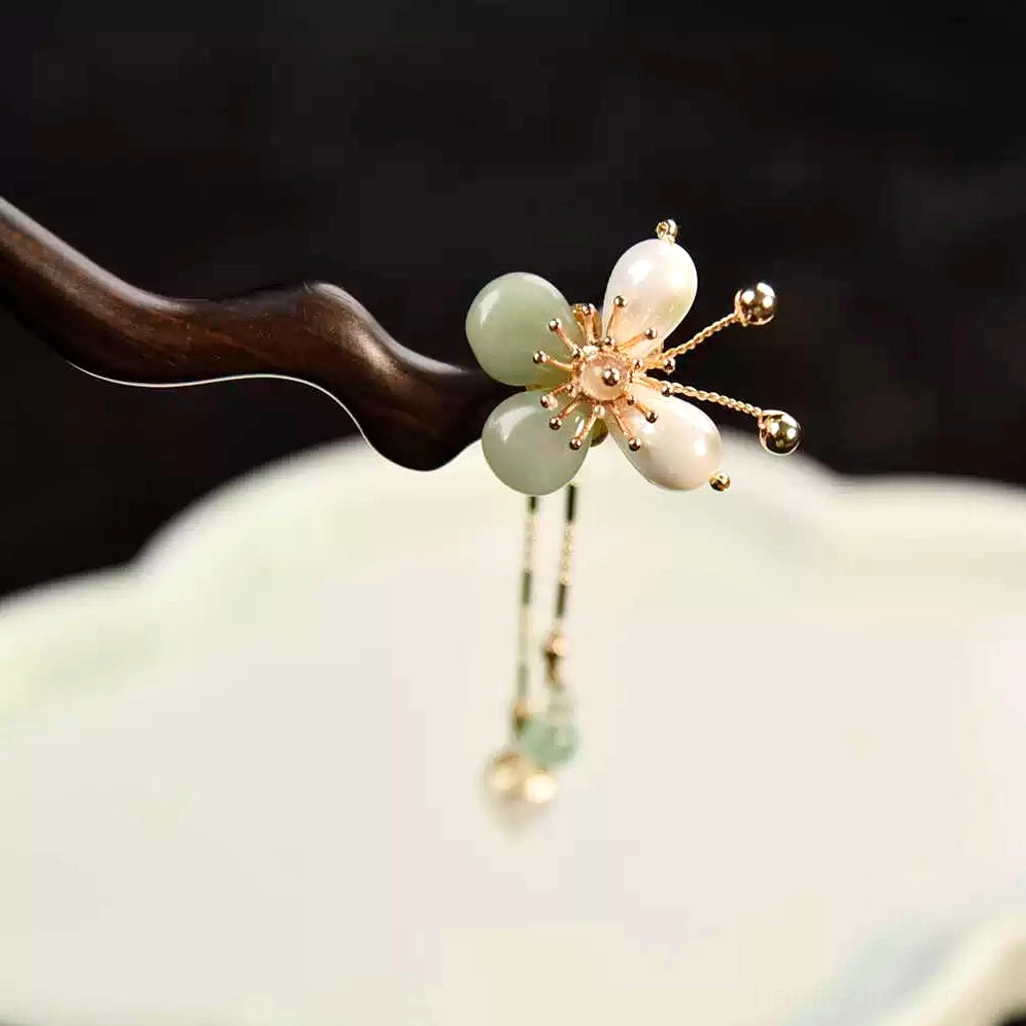 Traditional Chinese plum blossom hair stick beside a cloud-shaped ceramic tray, clearly showing the hanging gold-toned chain and decorative pendants
