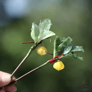 Traditional Chinese hair stick shown from an angled view with green pomelo leaves, dewy water-drop details, red wrapped stem, yellow fruit charms, and dark brown stick