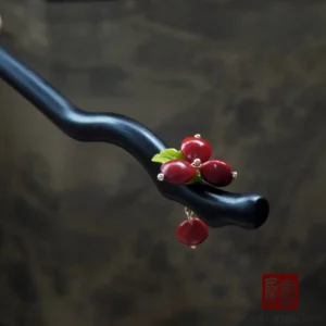 Traditional Chinese hair stick featuring clustered red bean berries, green foliage, gold-tone fasteners, a curved black wooden body, and a hanging red bead pendant